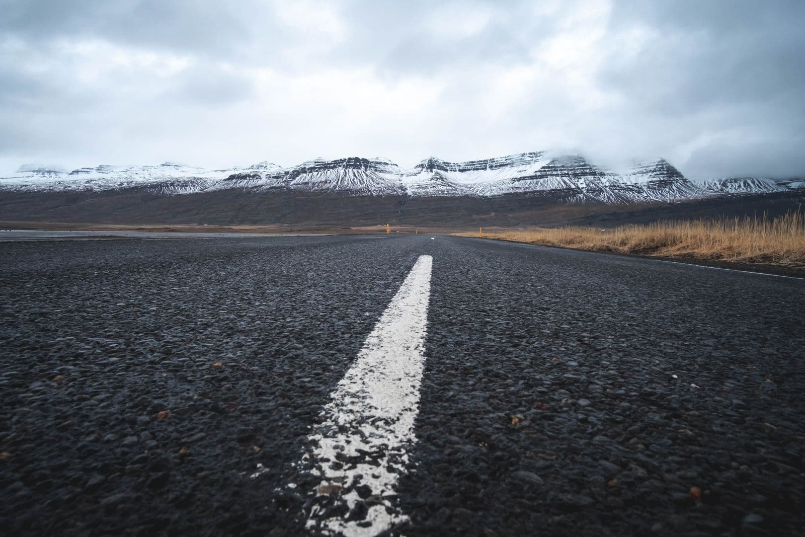 Empty road cutting through Iceland's green highland landscape under a dramatic grey sky